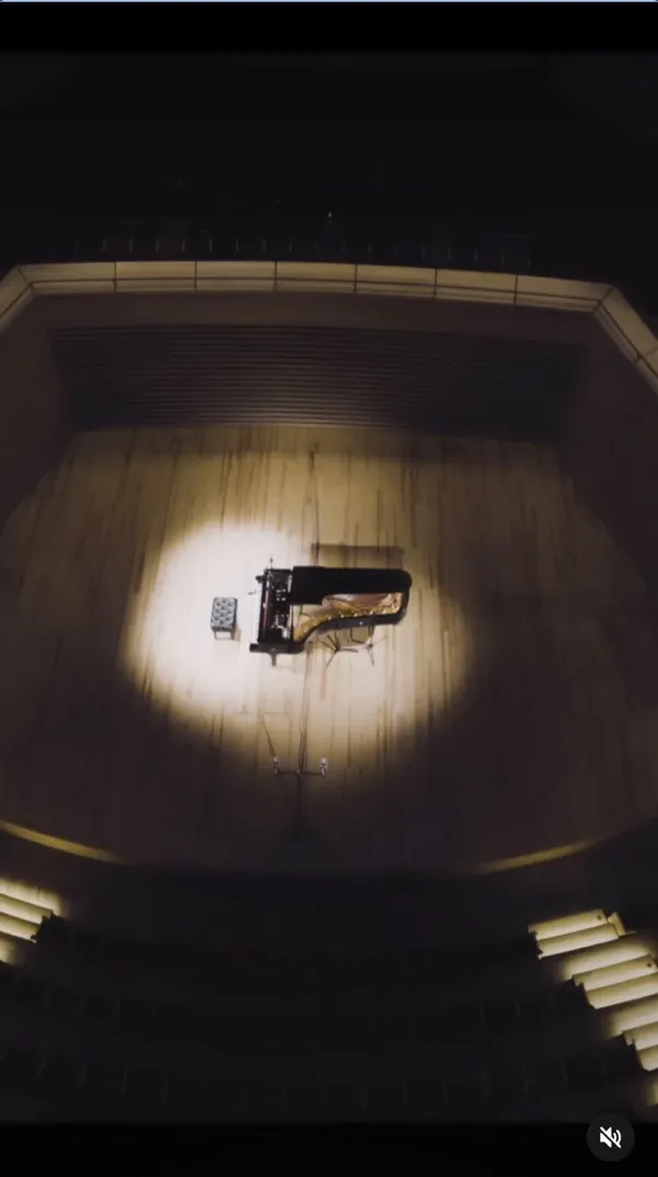 Reel: overhead view of a grand piano in a pool of light on the wooden stage of a dark concert hall