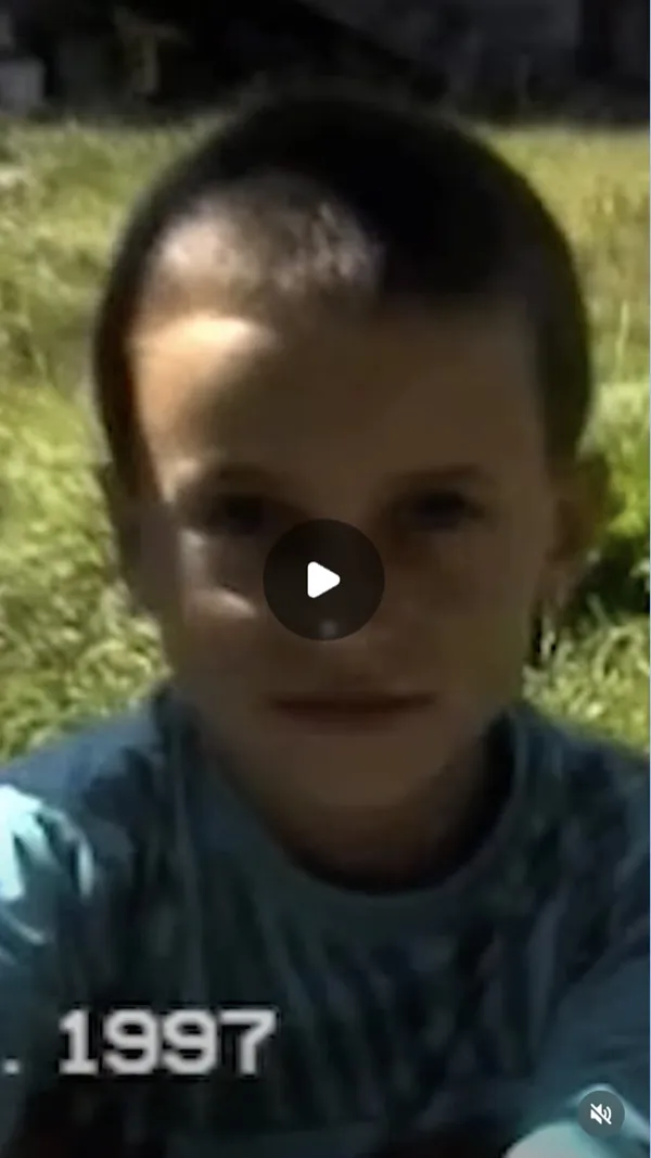 Reel: blurred archival frame of a short-haired child against grass, with a date in the corner