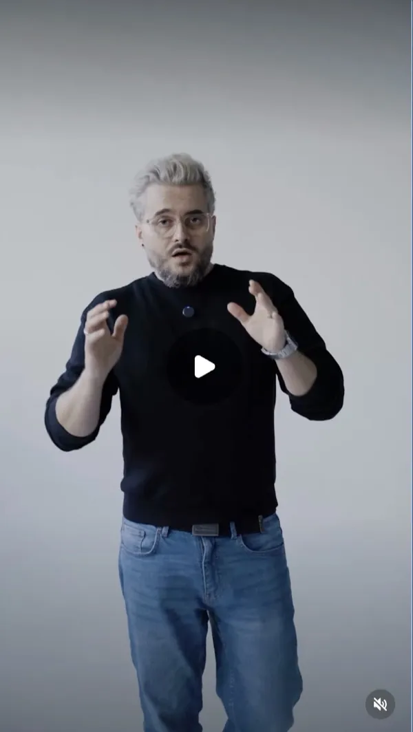 Reel: a man with light hair, beard and glasses in a black sweater talks to camera and gestures, grey backdrop
