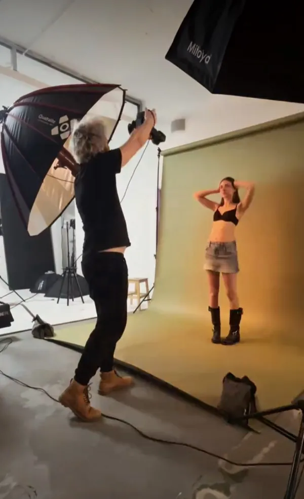 Behind-the-scenes reel: a photographer with a raised camera shoots a person in a denim skirt on an olive backdrop