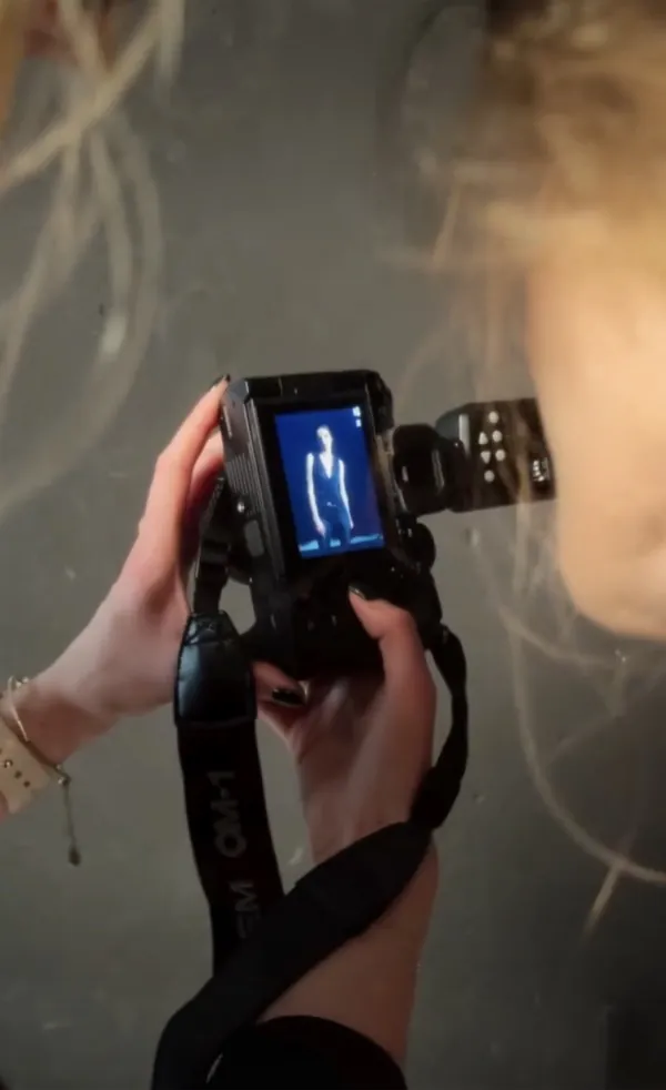 Behind-the-scenes reel: hands hold a camera whose screen shows a blue shot of a figure in a dark waistcoat