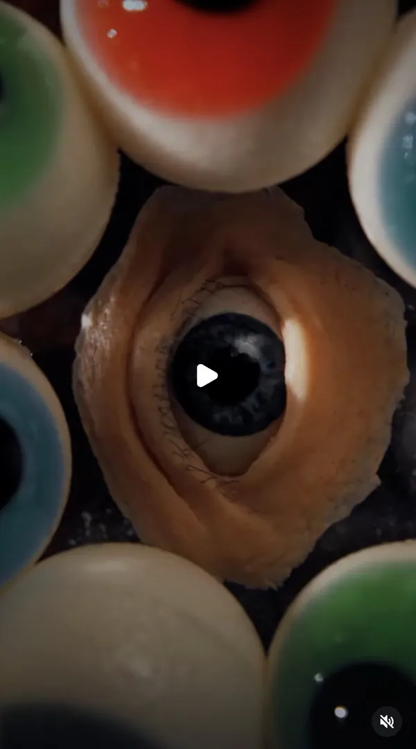 Reel: macro of a realistic eye in an orange setting among glossy coloured spheres that look like eyeballs