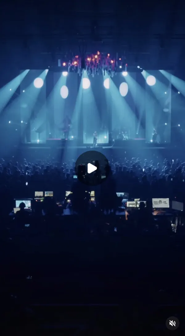Reel: concert stage under blue spotlight beams, the crowd and technicians' desks in the foreground