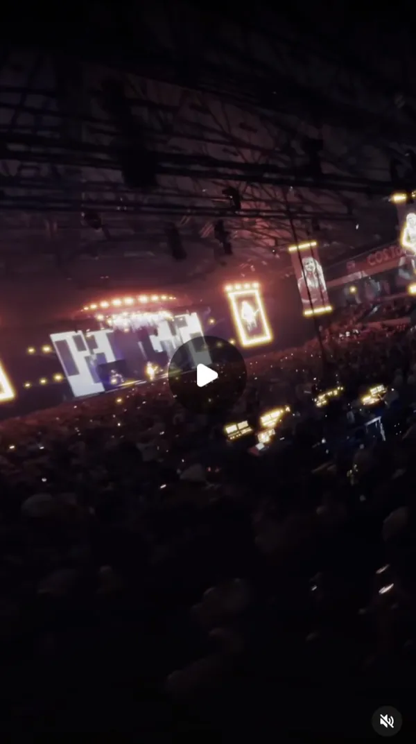 Reel: concert in a large arena seen from the audience, a dim stage with screens and lights above the crowd