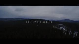 Film Homeland: aerial view of a dark coniferous forest and mountains under heavy clouds, title “Homeland”