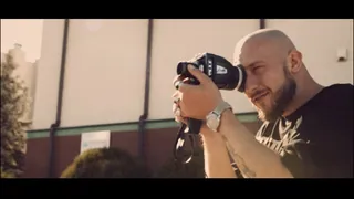 Music video Kortez — Niewidzialni: a bald bearded man looks through a film camera on a sunny day